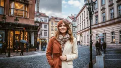 Žena stojí na historickém městském náměstí, půl na slunci a půl ve stínu.